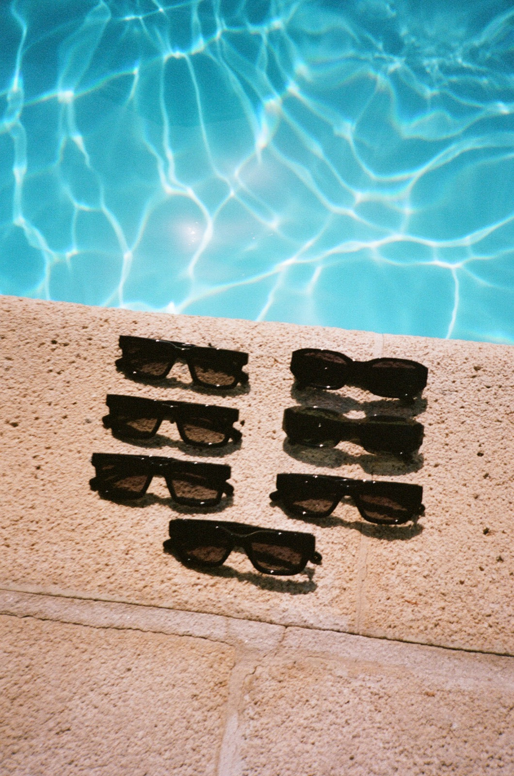 A wedding party’s black sunglasses lined up beside the swimming pool